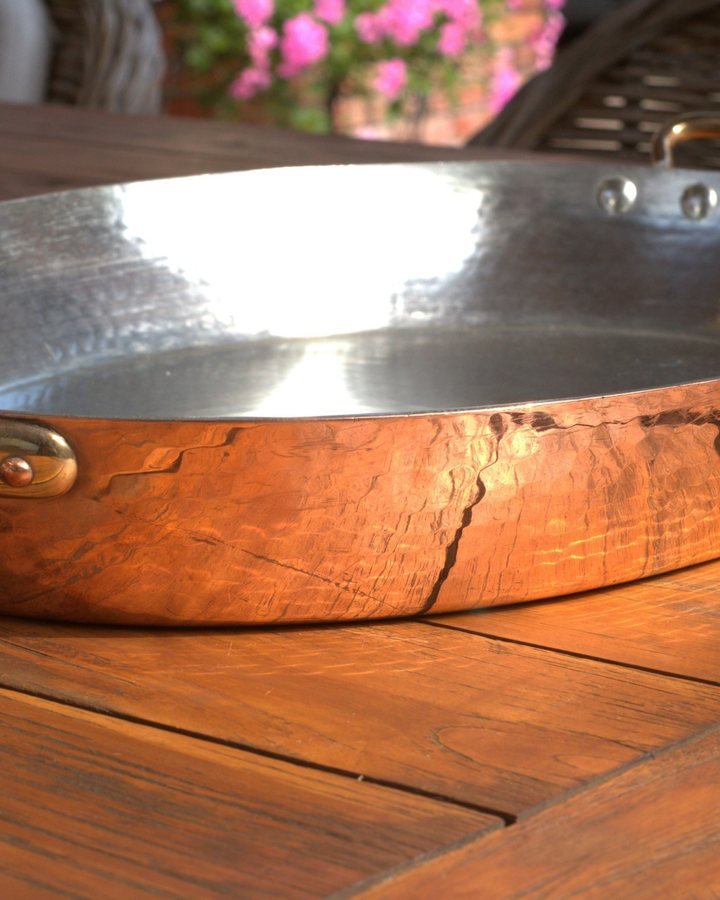 A hammered copper pan with brass handles on a wooden table