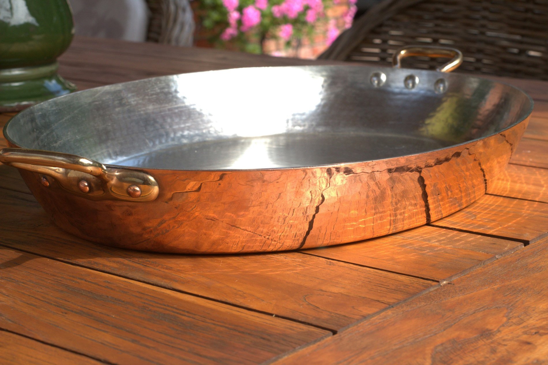 A hammered copper pan with brass handles on a wooden table