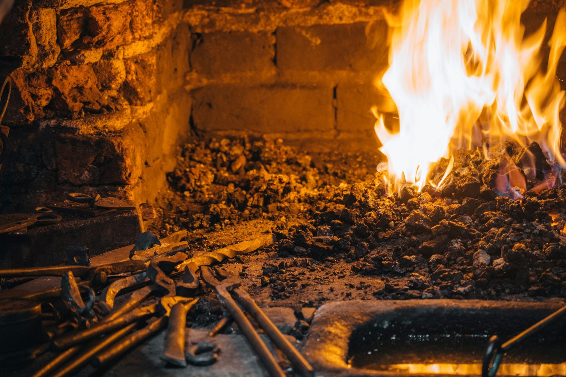 A forge fire with glowing coals and a smith's tongs and tools, as used to forge a small katana