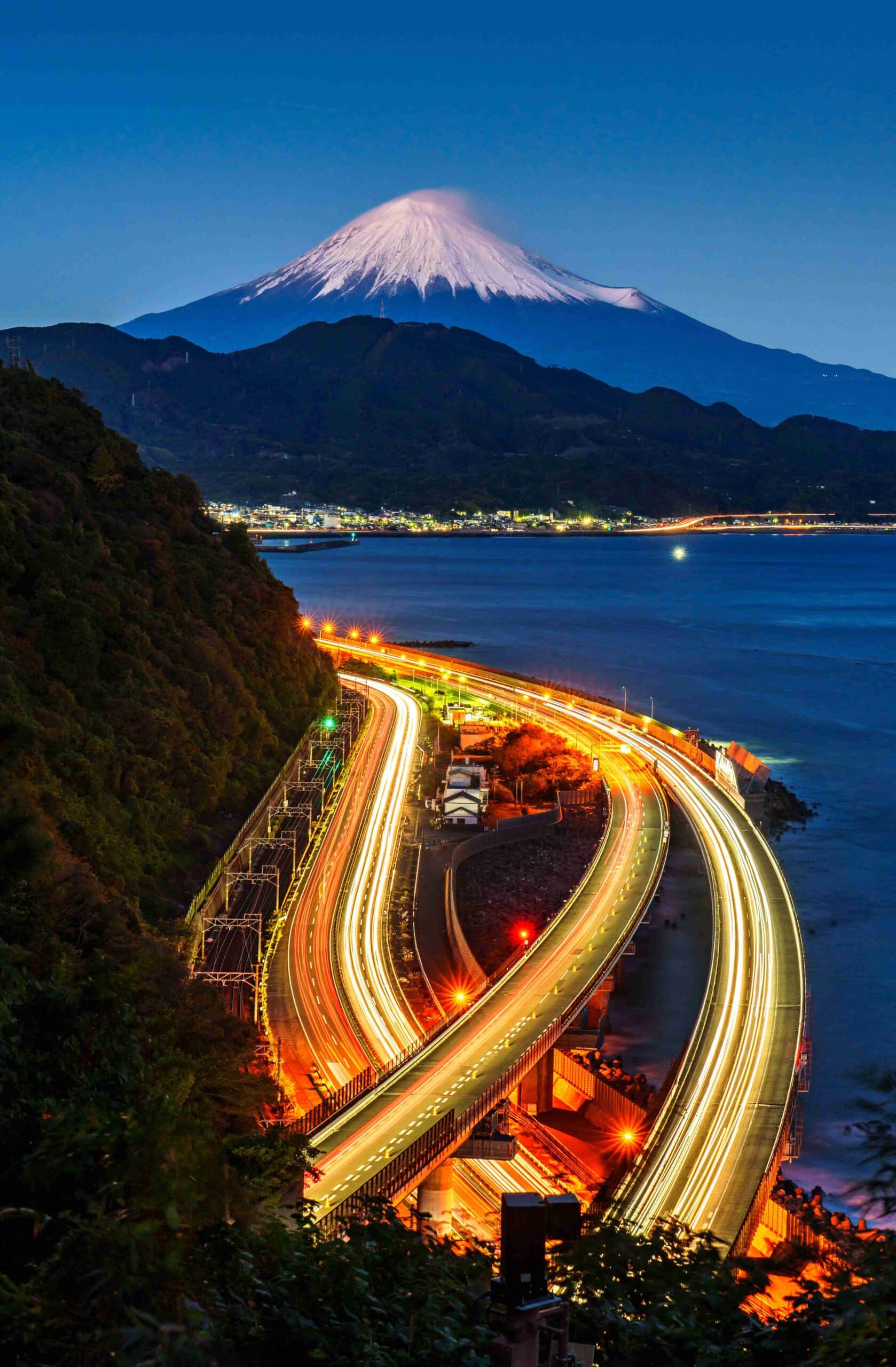 Long exposure curved highway light trails at night with city lights in the background, Japan