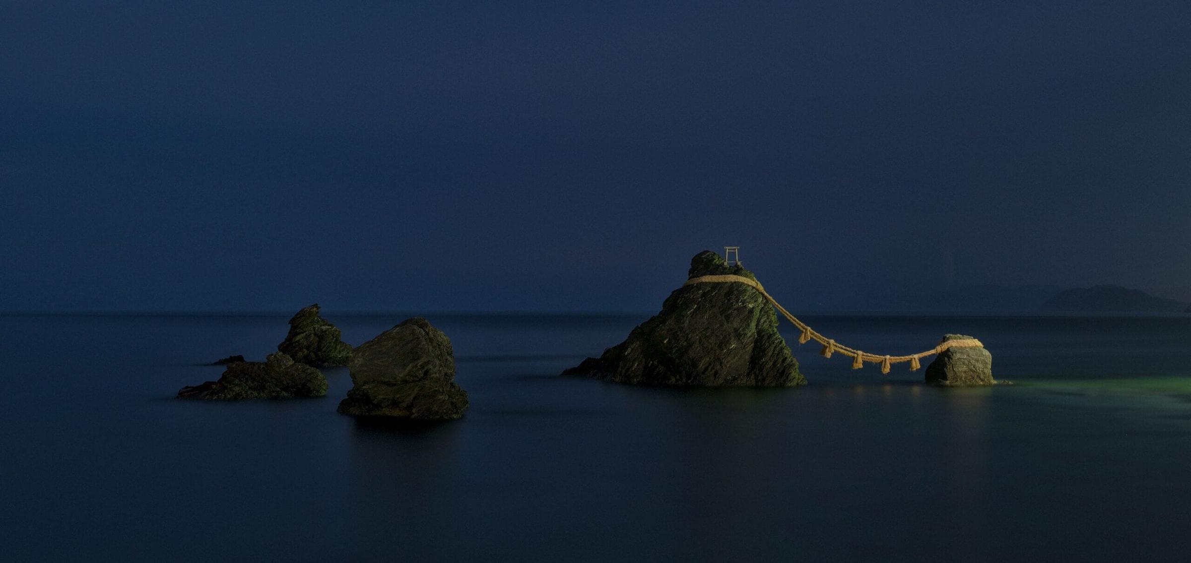 Dramatic sea stack rock island silhouetted against a dark dusk sky on Japan's coastline