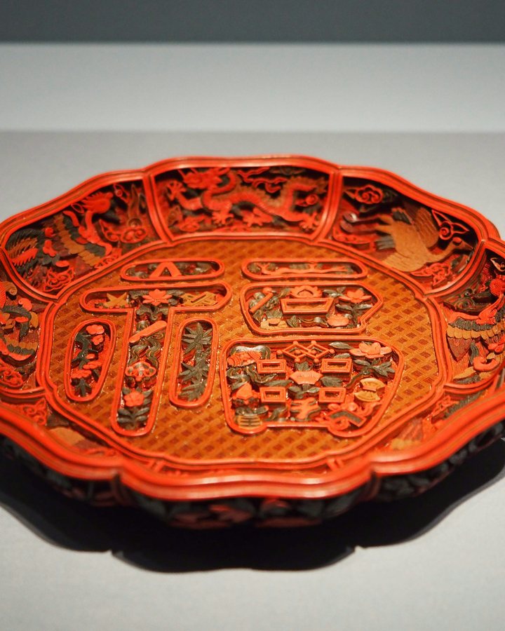 A carved red lacquer plate with an intricate raised pattern