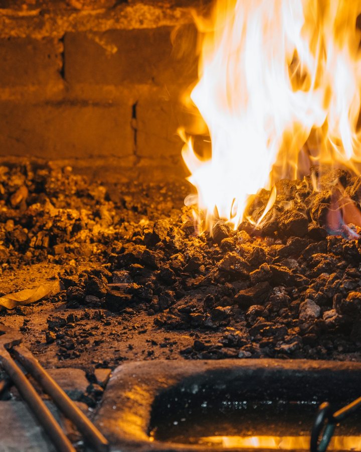 A forge fire with glowing coals and a smith's tongs and tools, as used to forge a small katana