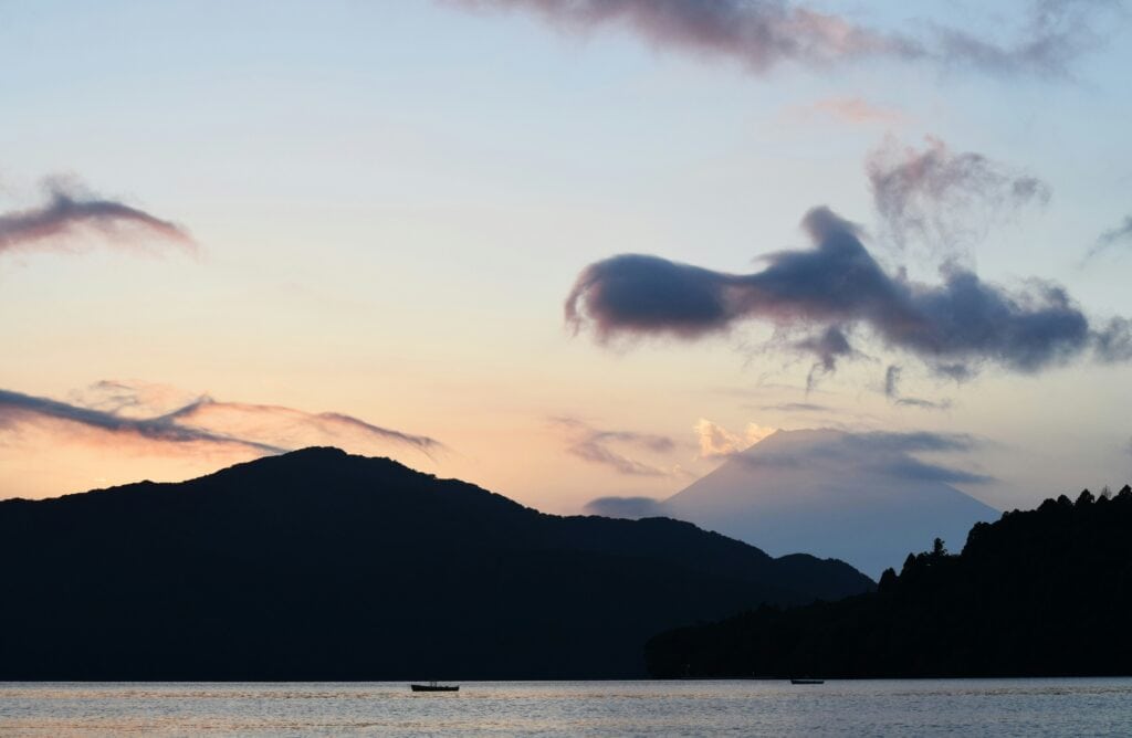 Mount Fuji at sunset seen from Lake Ashi with soft clouds and mountain silhouettes