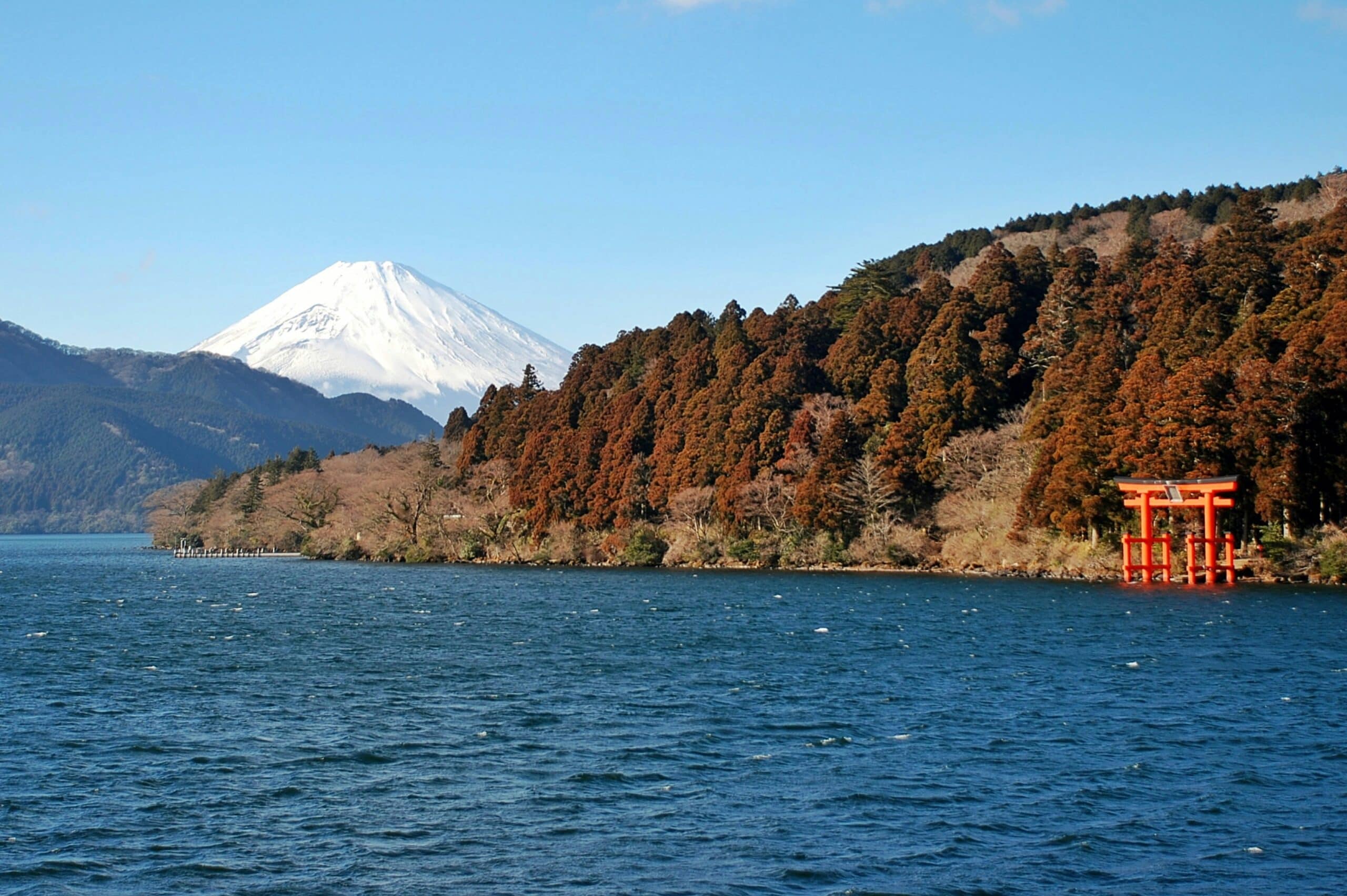 View of Mount Fuji from Lake Ashi in Hakone with red torii gate and forest shoreline