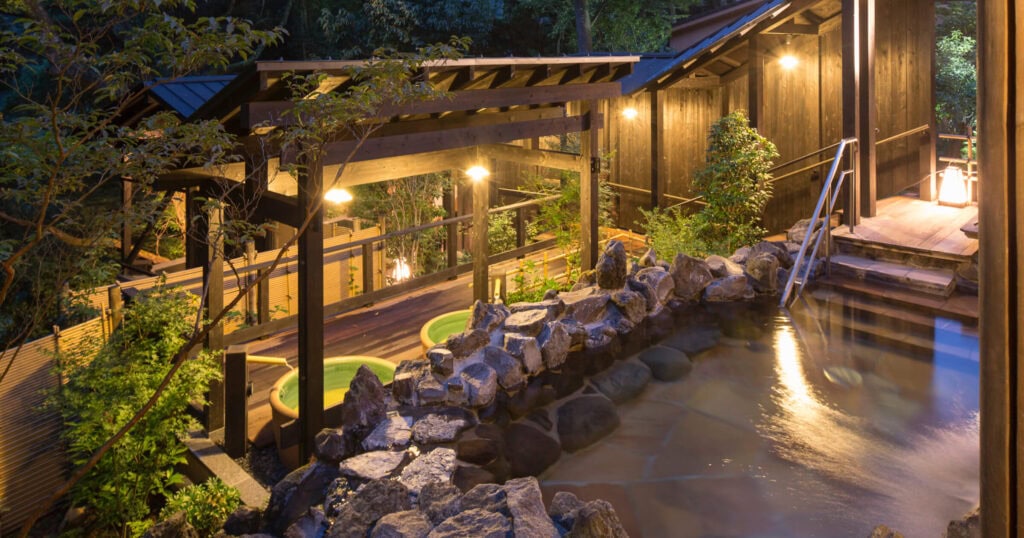 Outdoor hot spring bath at Yuryo Onsen in Hakone surrounded by trees and traditional wooden architecture near Tokyo